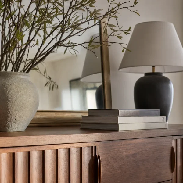 Piano di una credenza classica in legno allestito con specchio, lampada e vaso di rami, esempio di cosa mettere sopra la credenza